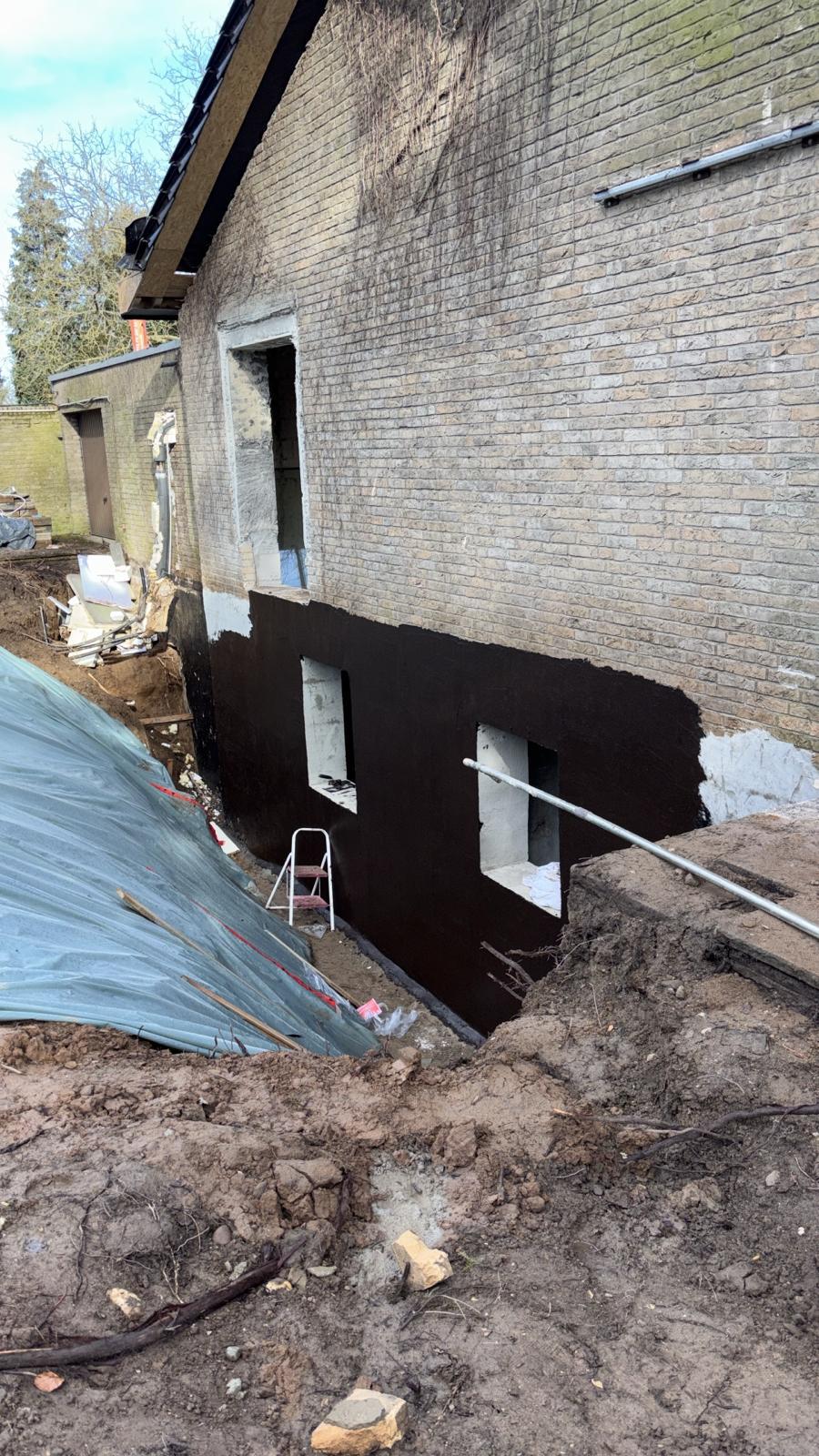 Kelleraußenwand mit neuer dunkler Beschichtung während der Bauarbeiten.