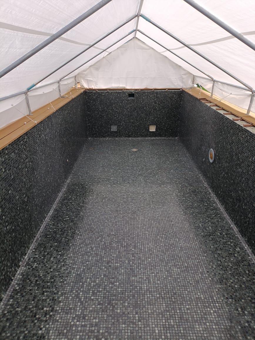 Poolbecken mit dunkler Mosaikauskleidung unter einer temporären Überdachung.