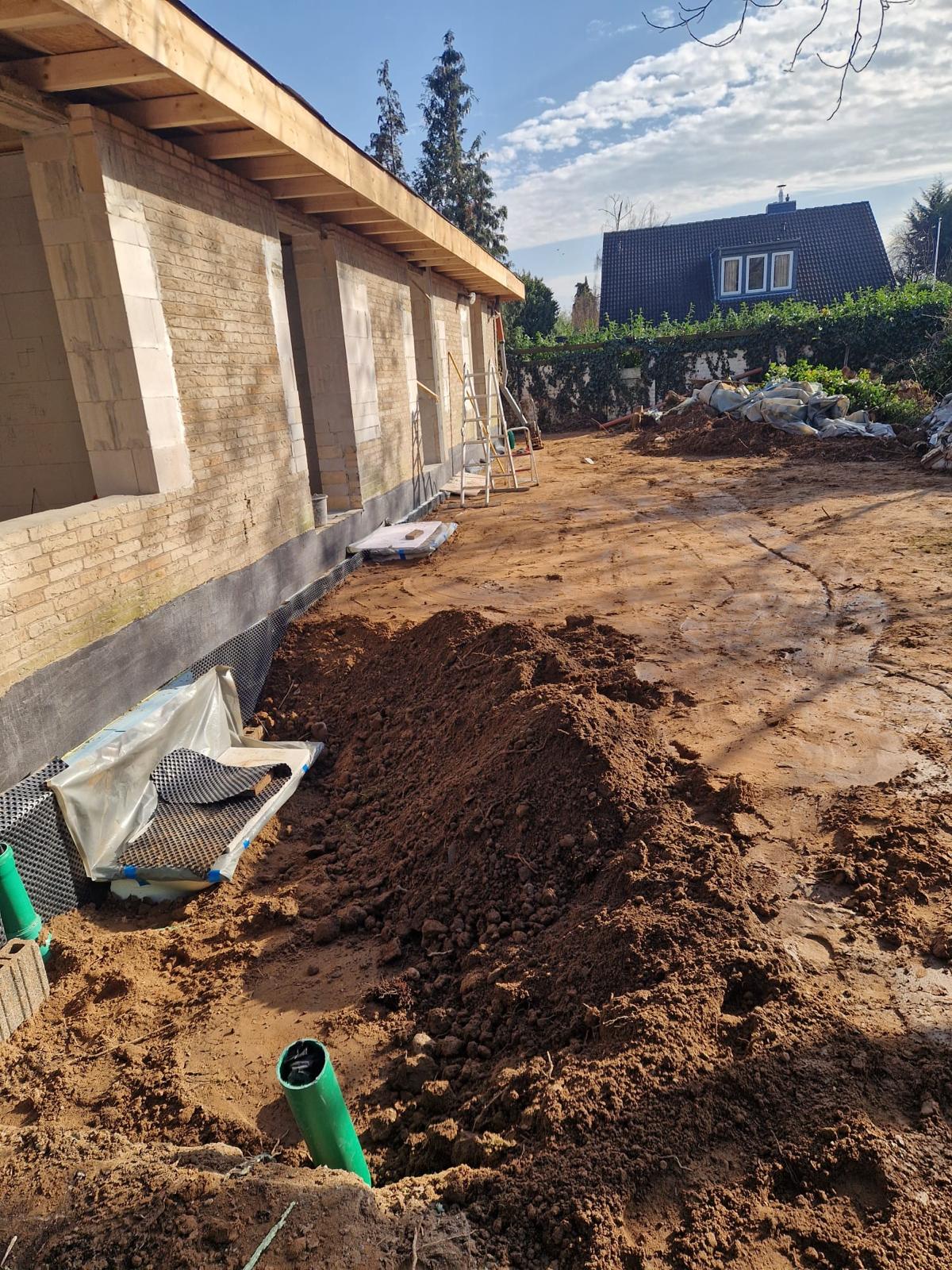 Außenansicht eines Gebäudes während des Umbaus mit bearbeiteten Wandöffnungen und verfülltem Erdreich.